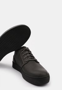 Scarpe in pelle nera con finitura liscia, punta rotonda e design con lacci. Caratterizzate da una suola in gomma nera testurizzata con un motivo ondulato.