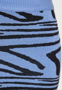 Kék kötött anyag fekete zig-zag csíkokkal, a tetején bordázott textúrával, az anyag többi része pedig sima felületű.
