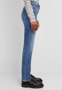 Vaqueros de pierna recta en denim azul medio, con cintura de talle medio, diseño de cinco bolsillos y dobladillo con vuelta. Combinados con mocasines negros.