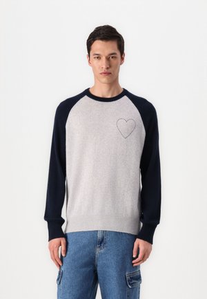 Light gray sweater with navy raglan sleeves, featuring a stitched heart detail on the chest. Soft knit fabric and ribbed cuffs.