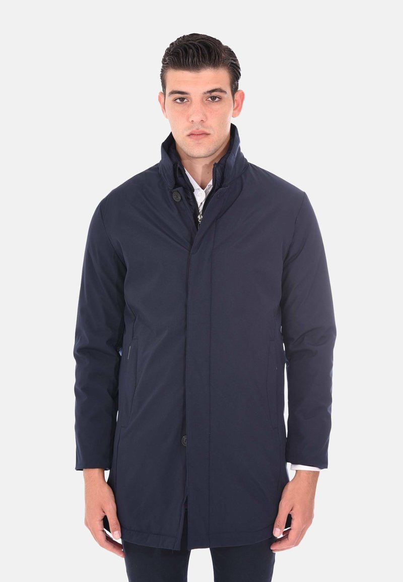 Giacca sintetica leggera di colore blu navy con colletto alto, maniche lunghe e chiusura anteriore con bottoni. Presenta tasche laterali e un design semplice.