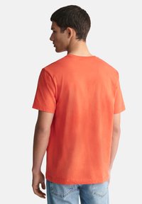 Kortermet t-skjorte i klar oransje bomull, med klassisk rund hals og standard passform, ensfarget bak uten mønstre eller dekorasjoner.