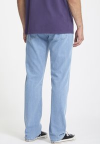 Jean en denim bleu clair avec une coupe droite. Pr�ésente des poches arrière et un léger dégradé. Porté avec des baskets noires.