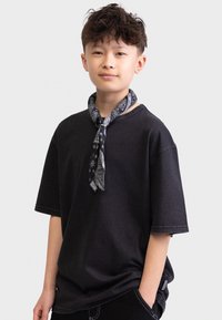 Schwarzes T-Shirt mit kurzen Ärmeln und lockerer Passform, kombiniert mit einem gemusterten grauen Schal, der um den Hals gebunden ist. Glatte Stofftextur, lässiges Design.