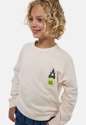 Sweatshirt beige clair avec col rond côtelé. Présente un graphique de flamme verte et une étiquette sur le thème du camping jaune à l'avant. Texture douce.