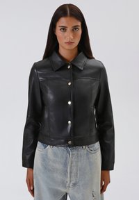 Giacca in pelle nera con colletto, bottoni a scatto e design croppato. Texture liscia con cuciture a contrasto. Inclusi tasche.