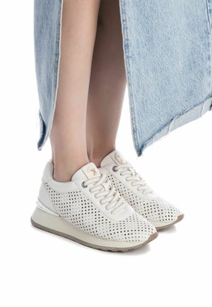 Zapatillas blancas perforadas con diseño de cordones, que cuentan con una suela acolchada, acentos en beige claro y una textura suave.