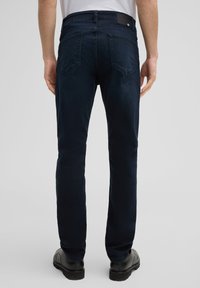 Ciemnoniebieskie dżinsy o wąskim kroju, z pięcioma kieszeniami, skórzaną naszywką na tylnym pasku i subtelnym wyblaknięciem dla uzyskania tekstury.