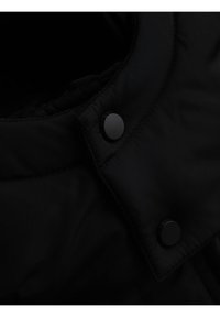 Acercamiento al cuello de una chaqueta negra con dos botones de presión redondos negros y detalles de costura visibles.