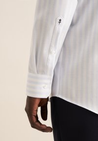 Camicia a righe blu chiaro e bianco con finitura testurizzata, polsino abbottonato e un piccolo ricamo di rosa nera sul maniche.