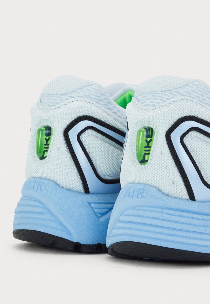 Zapatillas deportivas de color azul claro con tejido de malla, acentos negros y un detalle de logo verde. Presentan suelas acolchadas y un tacón texturizado.