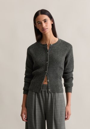 Donkergroene geribbelde cardigan met een ronde hals, knoopsluiting en lange mouwen, gecombineerd met grijs geruit wijde broek.