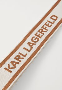 Nastro in tessuto beige con una striscia marrone, con "KARL LAGERFELD" tessuto in lettere maiuscole in grassetto. Texture liscia con una finitura pulita.