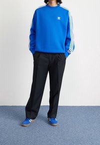 Sininen collegepaita, jossa valkoiset raidat hihoissa ja logo, yhdistetty mustiin housuihin ja sinisiin lenkkareihin, joissa valkoiset yksityiskohdat.