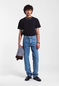 Musta lyhythihainen t-paita, vaaleansiniset suorat farkut, mustat kengät, kädessä harmaa ja ruskea kuvioitu villapaita. Yksinkertainen, rento asu.