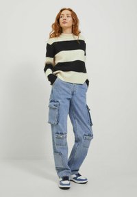 Maglione a righe nero e crema con collo rotondo, abbinato a jeans cargo azzurri chiari caratterizzati da molteplici tasche e una vestibilità rilassata.