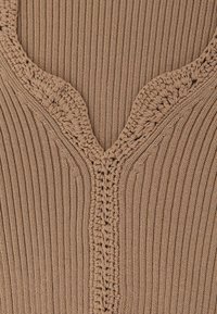Top beige lavorato a maglia con trama a coste, caratterizzato da una scollatura a V e dettaglio decorativo all'uncinetto. Il tessuto appare morbido e flessibile.