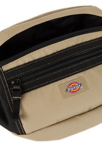 Custodia in tessuto beige con chiusura a zip nera e dettagli. Presenta una patch con logo e un design a doppio scomparto. Texture resistente e forma rettangolare.