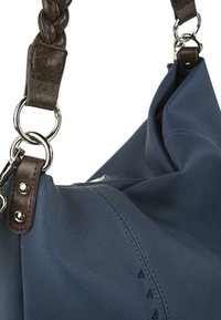 Bolso de tela azul con una correa de cuero trenzado marrón, herrajes plateados y un exterior texturizado con detalles de costura.