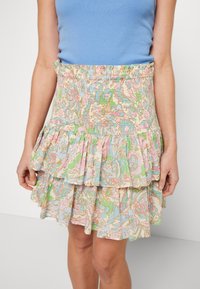 Jupe mini à motifs floraux dans des couleurs pastel, dotée d'une taille smockée et de volants empilés. Fabriquée en tissu léger avec une texture douce.