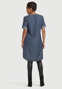 Denim tuniek met korte mouwen, opgerolde manchetten en een afgeronde zoom, gecombineerd met zwarte nepleer leggings en enkellaarsjes.