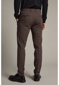 Bruna skräddarsydda byxor med en slät yta, med dubbla bakfickor och en smal passform. Matchas med svarta läderskor.