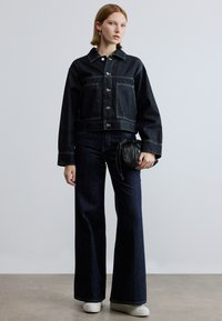 Sötét farmer rövidített dzseki ezüst gombokkal és nagy zsebekkel, széles szárú sötét farmerral és egy kis fekete táskával párosítva. Fehér sportcipő egészíti ki a megjelenést.