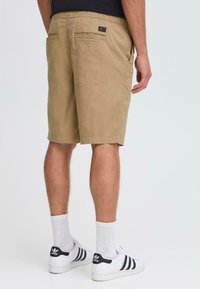 Khaki shorts med elastisk midjebånd, baklommer og syddsøm. Kombinert med hvite sokker og svart-hvite joggesko.