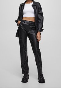 Pantalons en simili cuir noir à coupe ajustée, avec deux poches avant et des jambes droites. Associés à un crop top blanc côtelé et des bottes noires.
