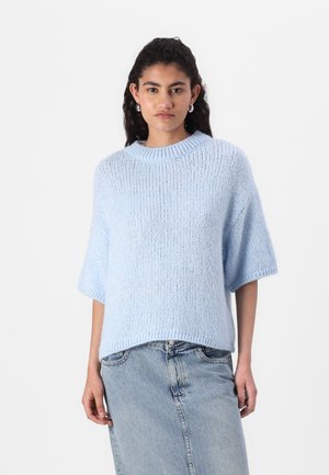 Pulover tricotat de culoare albastru deschis, cu o croială lejeră, mâneci scurte și guler rotund, purtat împreună cu o fustă din denim. Textura moale este evidentă.