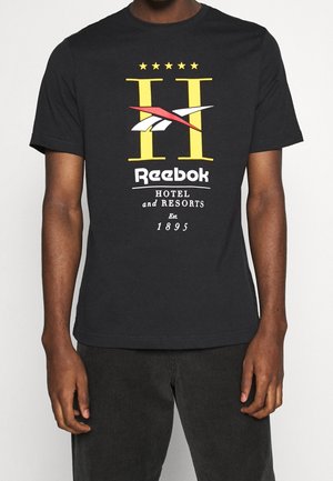 Camiseta negra con gran letra amarilla H, logo de Reebok en rojo y blanco, texto "Reebok Hotel and Resorts Est. 1895" en el frente.
