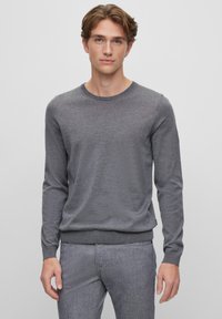 Grauer Langarmpullover mit rundem Hals, weichem Material und geripptem Saum. Kombiniert mit hellgrauen, maßgeschneiderten Hosen.