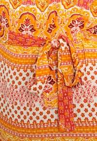 Mnohobarevná látka s květinovými vzory v červené, oranžové a žluté barvě se středovým detailem ve tvaru motýlka a kontrastními pruhy.