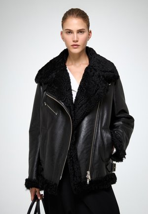Must mustastikuning nahktagi pehme musta shearling krae ja mansettidega. Omab tõmblukuga taskuid ja vöökoha juures solki.