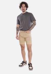 Shorts in denim beige con una vestibilità slim, abbinati a una maglietta grigia a maniche corte. Presentano un design classico e dettagli di cucitura visibili.