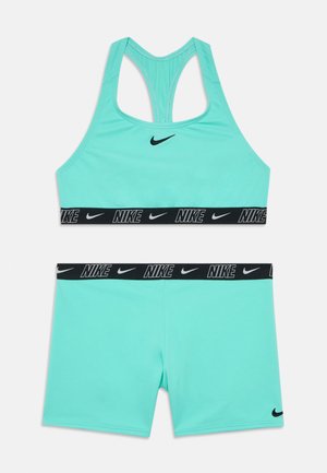 Nike sports bra and shorts set in light teal. Bra features a racerback design, black logo, and branded elastic band. Shorts have a matching color and band.