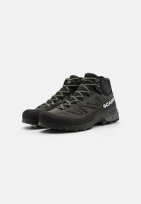Czarne buty trekkingowe o wysokim fasonie, z teksturowanym materiałem wierzchnim, zielonymi sznurówkami i solidną, antypoślizgową podeszwą. Łączy je logo na boku.