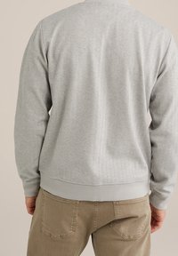 Šedá mikina vyrobená z měkké, strukturované látky s žebrovanými manžetami a lemem. Má jednoduchý, klasický design bez viditelných log a vzorů.