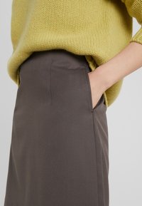 Pull en tricot jaune à coupe ample sur une jupe brune cintrée avec poches latérales et texture lisse.