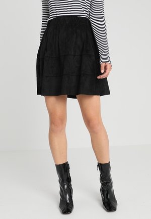 Gonna a strati in suede nera con cintura elastica, abbinata a una maglietta a maniche lunghe bianca e nera a righe e stivaletti neri con zip alla caviglia.