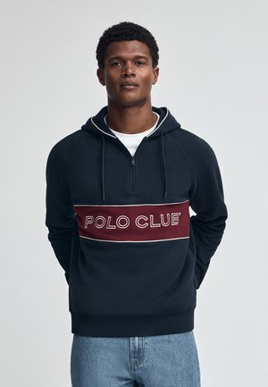 Felpa con cappuccio blu navy con zip a quarto, caratterizzata da una striscia orizzontale bordeaux con "POLO CLUB" in lettere bianche. Vestibilità casual, texture morbida.