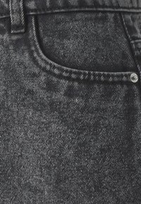 Tmavě šedá denímová látka s jemnou texturou, obsahující přední kapsu, kontrastní švy a kovový knoflíkový detail.