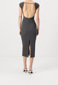 Šedé upnuté šaty s krátkými rukávy, otevřeným zády, postranním rozparkem a hladkou texturou. Tkanina se přizpůsobuje tělu a vytváří elegantní siluetu.