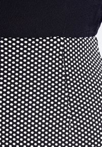 Černý textil s texturovanou, žebrovanou horní částí a spodní částí s bílým puntíkovaným vzorem na černém pozadí.