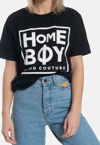 Svart bomullströja med stor vit text "HOME BOY" och "LOUD COUTURE" i fet stil. Matchas med högmidjade ljusblå jeans.