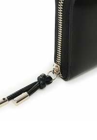Cartera de cuero negra con un cierre dorado. Presenta un detalle de borlas trenzadas unidas a un anillo plateado. Textura suave con bordes cosidos.
