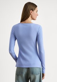 Ανοιχτό μπλε ριμπ πουκάμισο με μακριά μανίκια, διαθέτει στρογγυλή λαιμόκοψη, στενή εφαρμογή και πλευρικές σχισμές, συνδυασμένο με τζιν σε ανοιχτό ξεβάμμα.