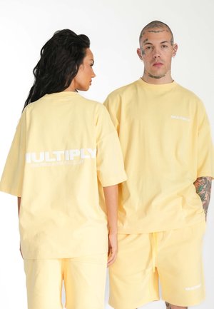 T-shirt oversize in cotone giallo e pantaloni abbinati, con il logo "MULTIPLY" in bianco sul retro, caratterizzati da una vestibilità rilassata e maniche corte.