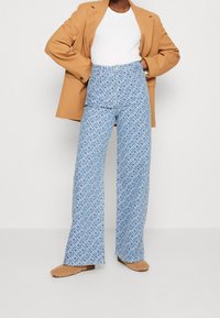 Jeans blu a vita alta con motivo a fantasia e design a gamba larga, abbinati a una maglietta bianca e un capo esterno beige, completati da calzature beige slip-on.