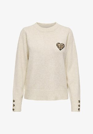 Pull crème à manches longues, avec des poignets côtelés, un col rond, et un patch en forme de cœur avec un imprimé léopard sur la poitrine. Détails en boutons aux poignets.